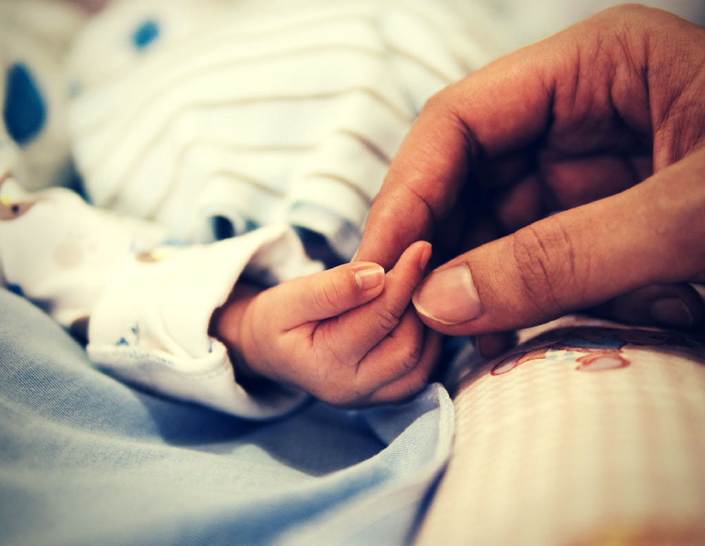 Newborn's hand gripping adult's finger